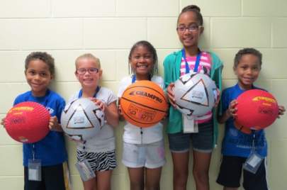 Children holding basketballs and kickballs